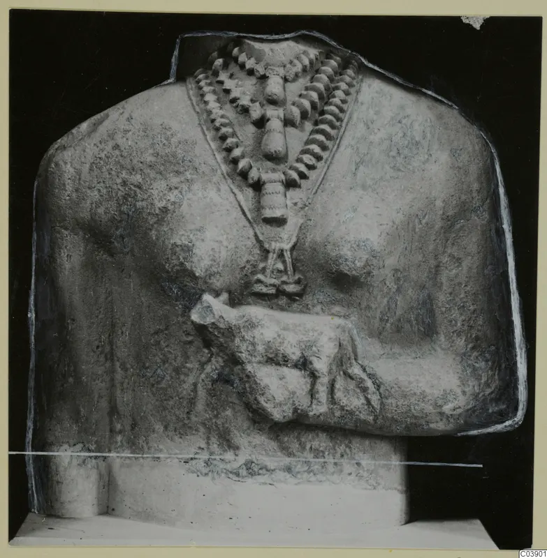 Limestone sculpture fragment of a figure's upper body, with a bead necklace and a small carved animal at the chest