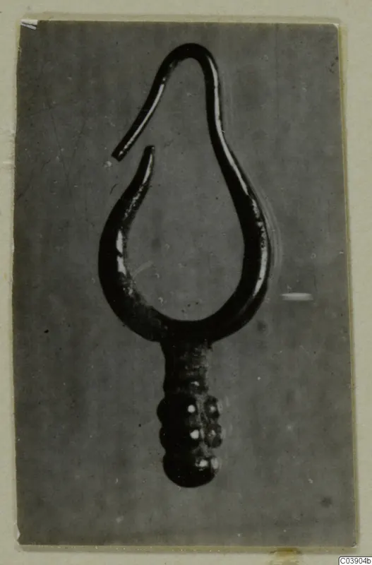 Close-up photograph of a single gold loop-shaped find from Amathus tombs, with a hooked open end and a beaded lower stem