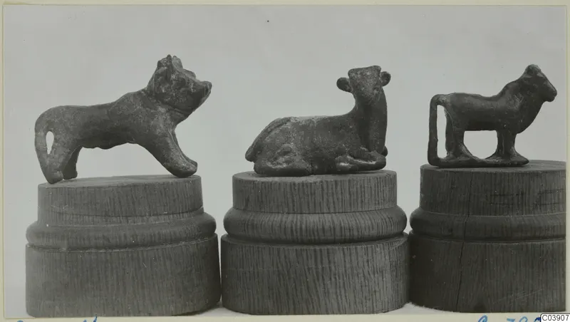 Three small bronze animal figurines, each on a turned wooden stand, photographed side by side against a grey backdrop