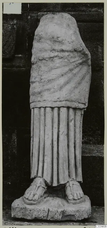 Limestone statue of a standing draped figure, head and arms missing, set on a rectangular base