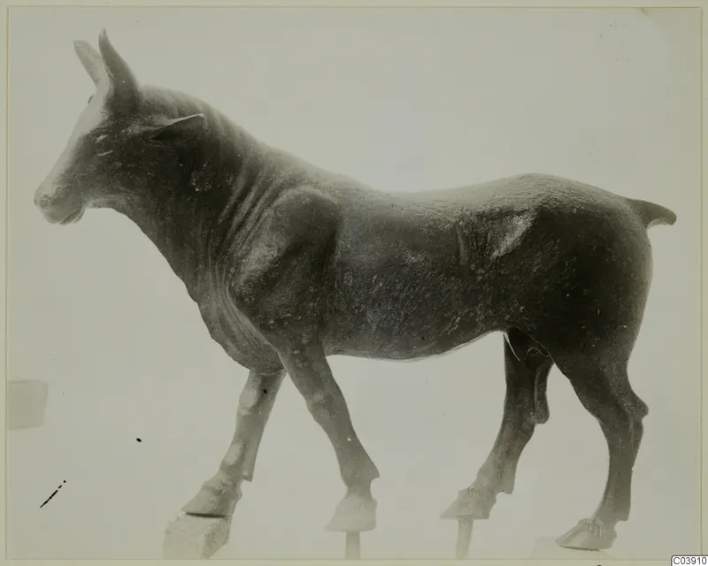 Bronze figurine of a standing donkey or mule, seen from the side against a pale background