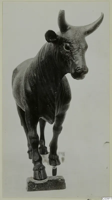 Bronze figure of a bull standing on a small stone base, head turned to one side.