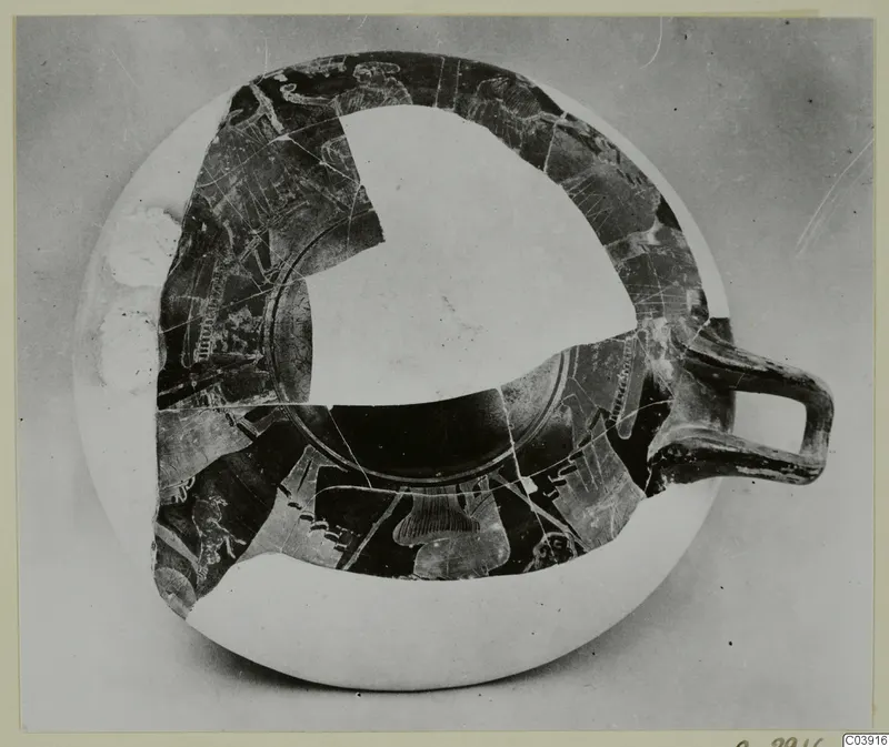 Shallow painted pottery bowl with a single loop handle, seen from above, with pale figure outlines and white restored areas.