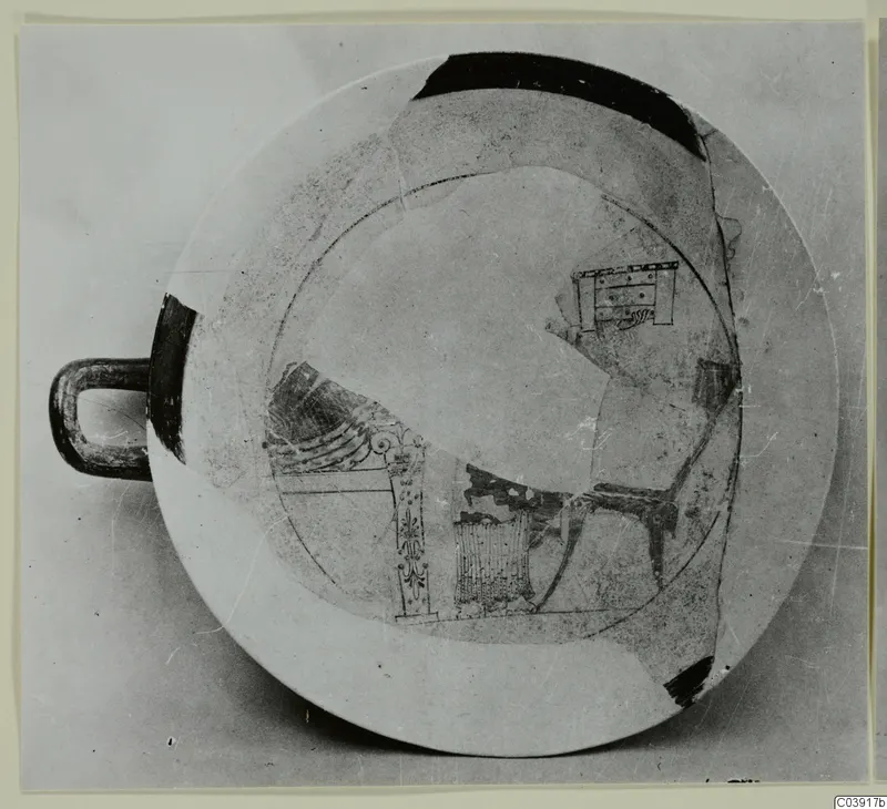 Shallow pottery bowl with a loop handle and dark painted motifs on a pale ground, seen from above