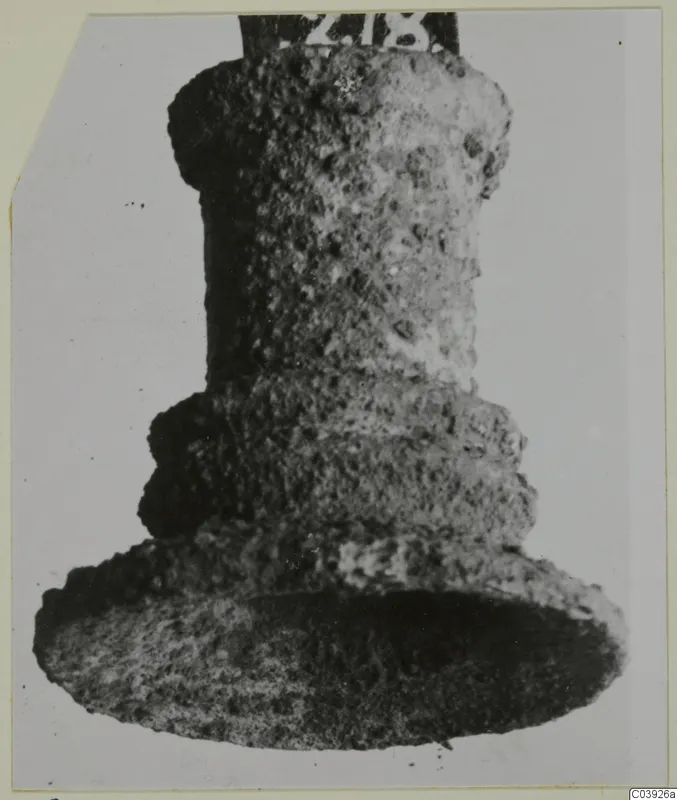 Bronze mounting fragment: a short cylindrical piece with a stepped collar and broad flared foot, shown upright against a grey backdrop.