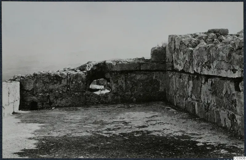 Ruined stone walls and a flat floor surface at Vouni, with a small opening in the lower wall and hazy hills beyond
