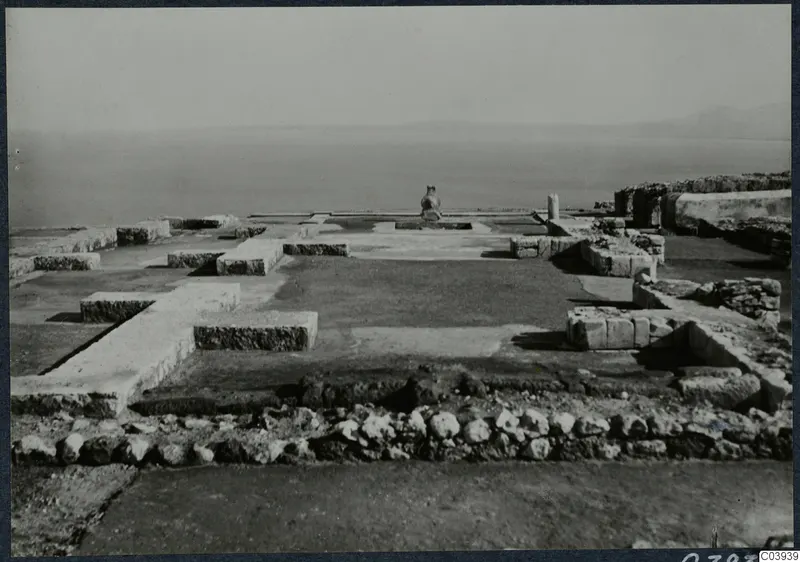 Low stone wall foundations and paved floors at Vouni palace, with a large jar on a base and the sea beyond