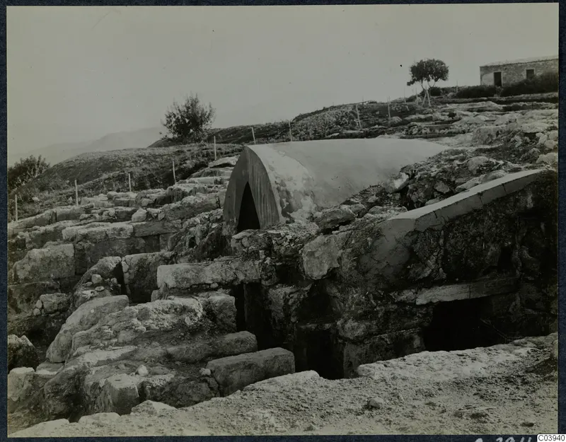 Stone walls and steps at Vouni with a curved white cover over an arched opening, and a stone building beyond.