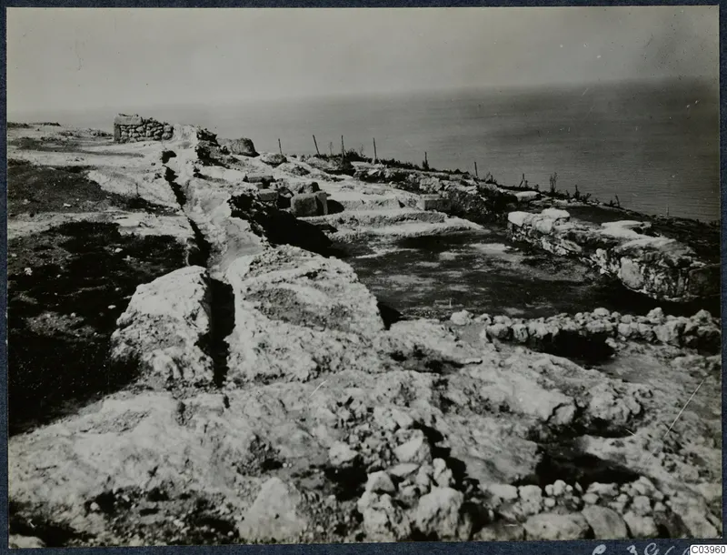Ruined stone walls and scattered stone blocks on a rocky coastal headland at Vouni, with the sea beyond