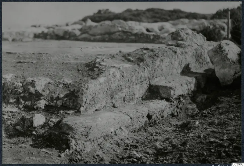Excavated stone walls and stepped masonry at Vouni, with low rubble walls and a hillside behind.