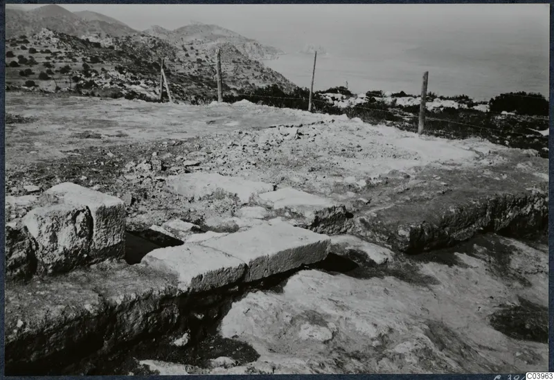 Stone foundations of the Temple of Athena at Vouni, with a fenced hillside and the sea beyond.