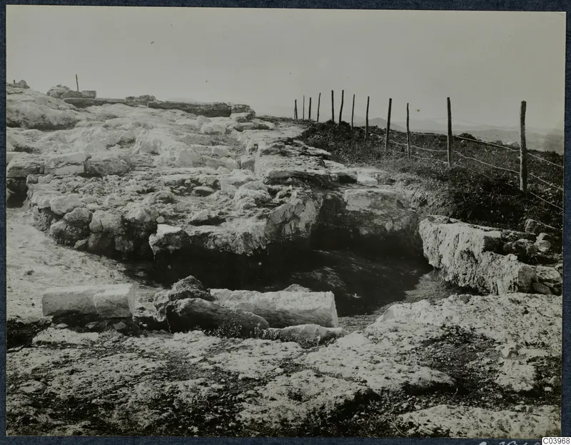 Ruined stone remains at Vouni Temple of Athena, with a wire fence along a hilltop and distant hills