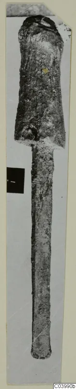 Corroded bronze tool with a broad socketed head and a long tapering shank, from the Vrysi tou Barba tombs at Lapithos