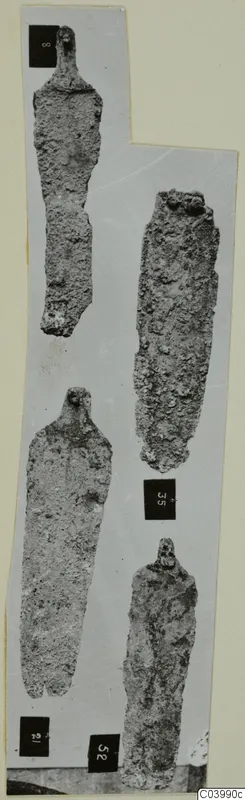 Four corroded bronze tools with tangs and long narrow blades, photographed on a grey card with number labels