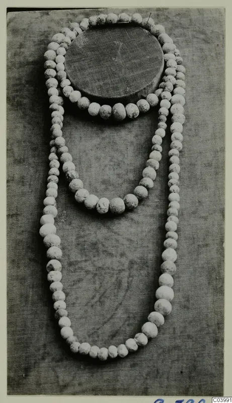 Three strands of pale, speckled beads of graduated sizes laid out on grey cloth