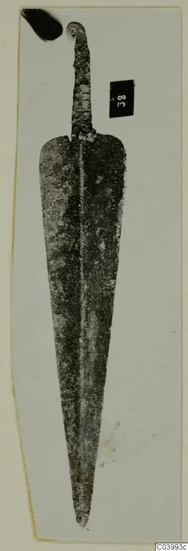 Corroded metal weapon blade from Lapithos, Vrysi tou Barba tombs, photographed on a pale card