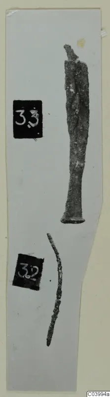 Two corroded metal tools on a grey card strip: one long with a flared base, a thin curved fragment below, beside number labels.
