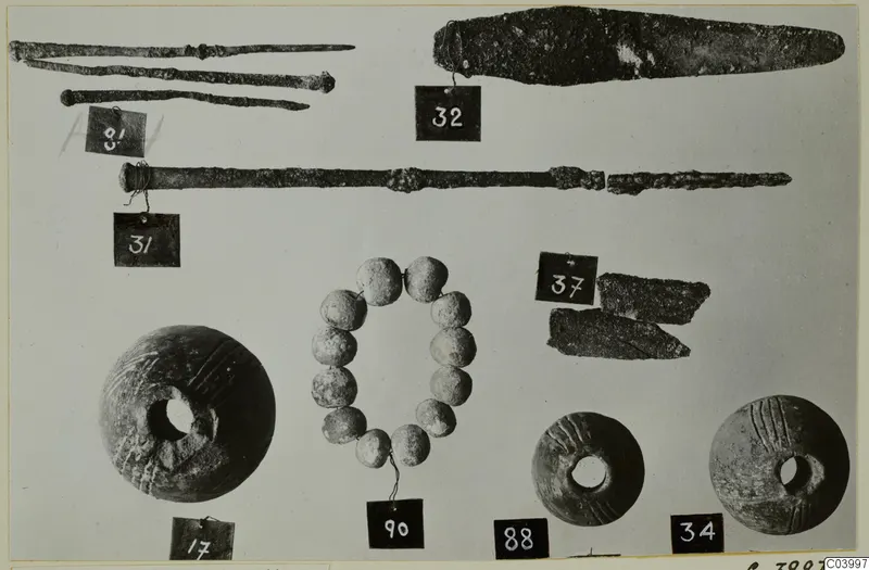Bronze tools, rods, a blade and beads from Lapithos Tomb 322 D, laid out with numbered tags