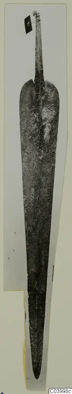 Long corroded metal blade with a tapering tang, photographed upright on a mounted card