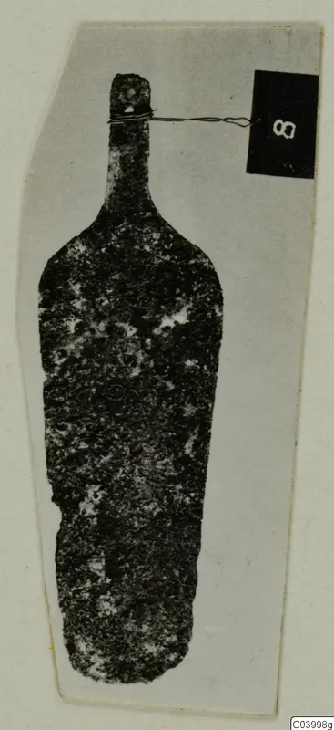 Corroded bronze tool from Lapithos Tomb 323 D, upright against a grey card, with a number label