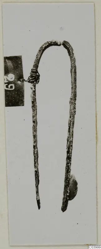 Corroded metal U-shaped implement with pointed ends, photographed on a pale card, from Lapithos Tomb 311A