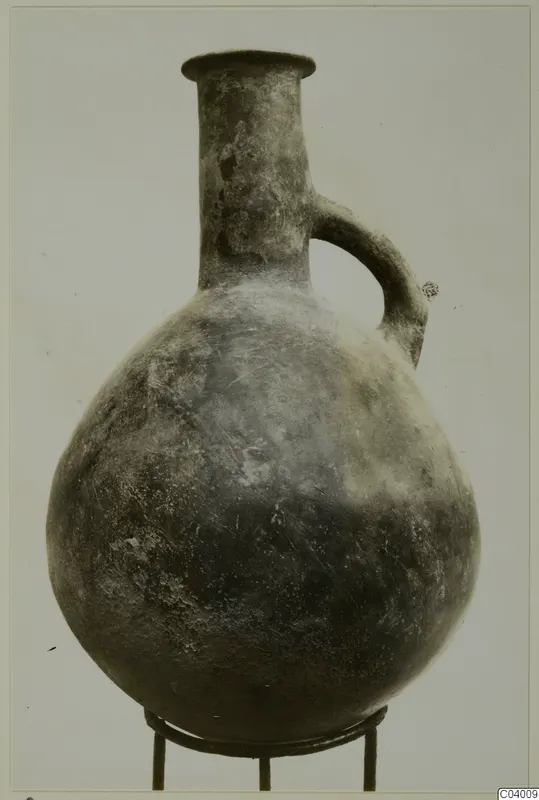 Red Polished III jug with a globular body, tall neck and single loop handle, standing on a metal stand.