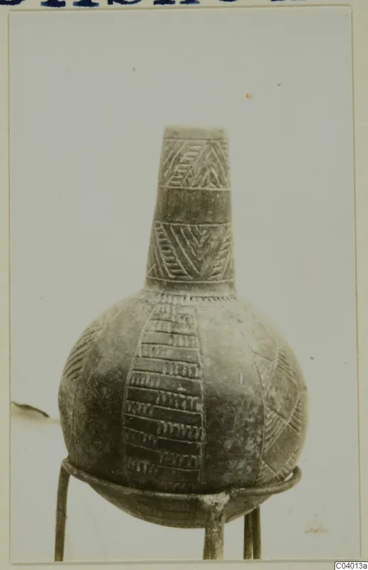 Pottery Red Polished II jug with incised geometric bands, shown on a three-legged metal stand