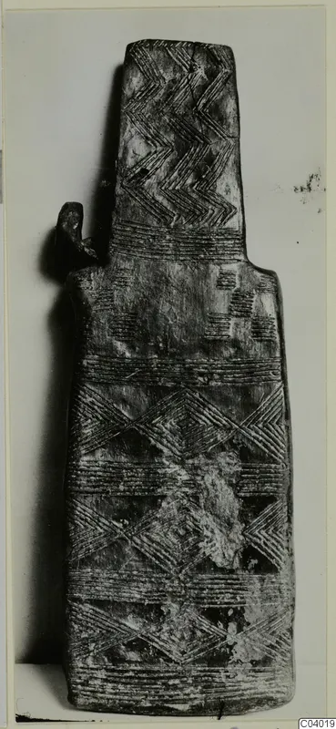 Flat idol-like object with incised chevron and band patterns, shown upright against a plain background