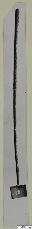 Long, slender metal tool photographed upright on a pale card strip.