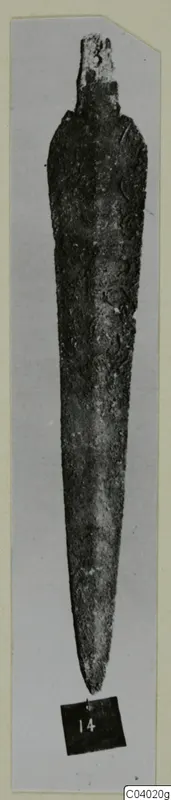 Long tapering bronze blade with a short squared end, photographed upright on a grey card mount