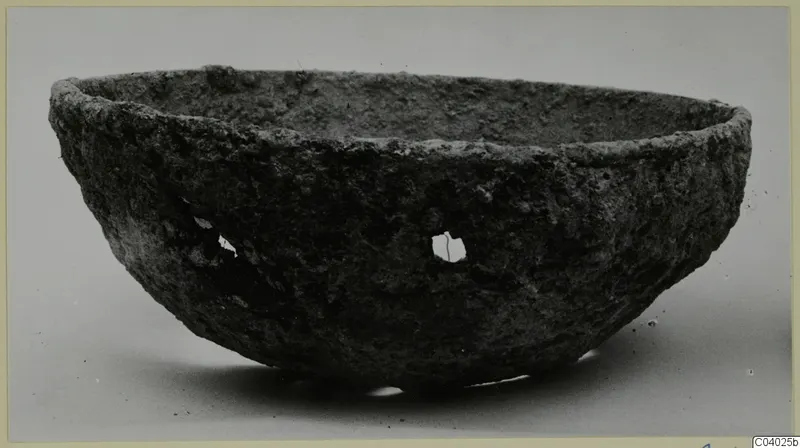 Rough-surfaced bowl with a thick rim and small openings in its side, photographed from the side