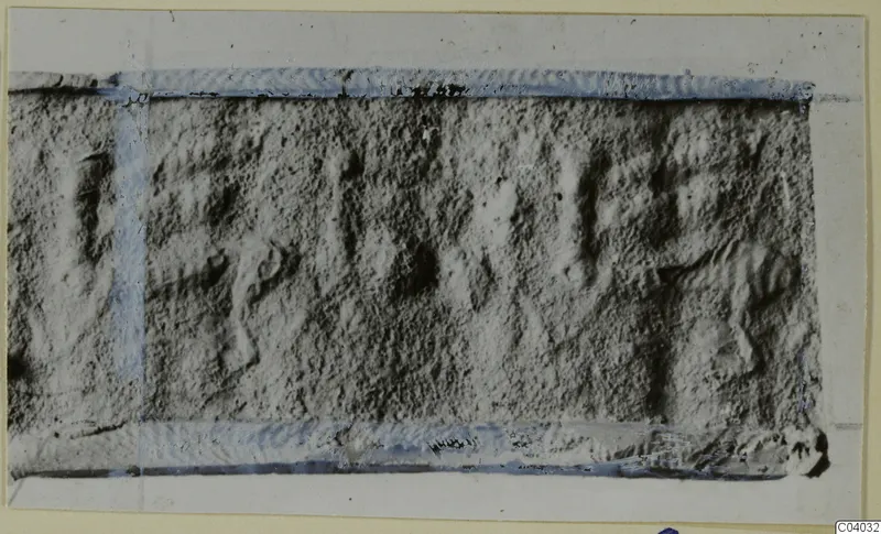 Rectangular grey stone object with incised marks or signs, edges taped in blue