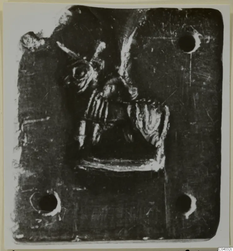 Square dark stone plaque with a raised figure in relief at its centre and holes near the corners