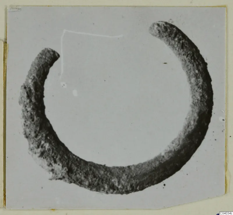 Corroded silver ring with a gap between its two ends, photographed on a grey card