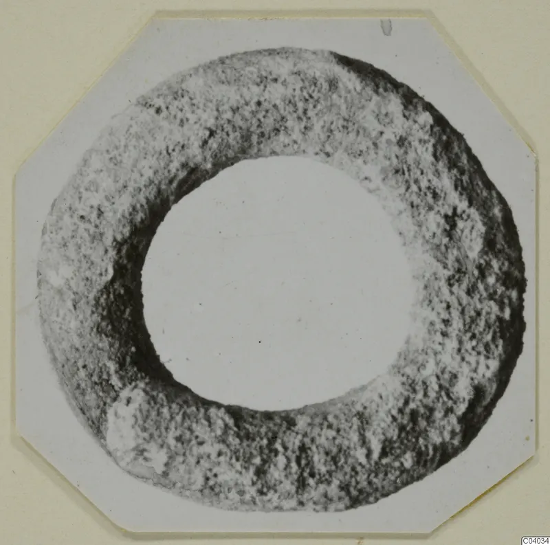 Lead ring-shaped object with a rough, pitted surface, seen face-on against a white card.
