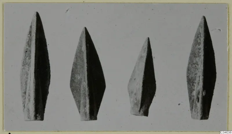 Four leaf-shaped metal weapon points standing in a row, tips upward, against a plain grey background.