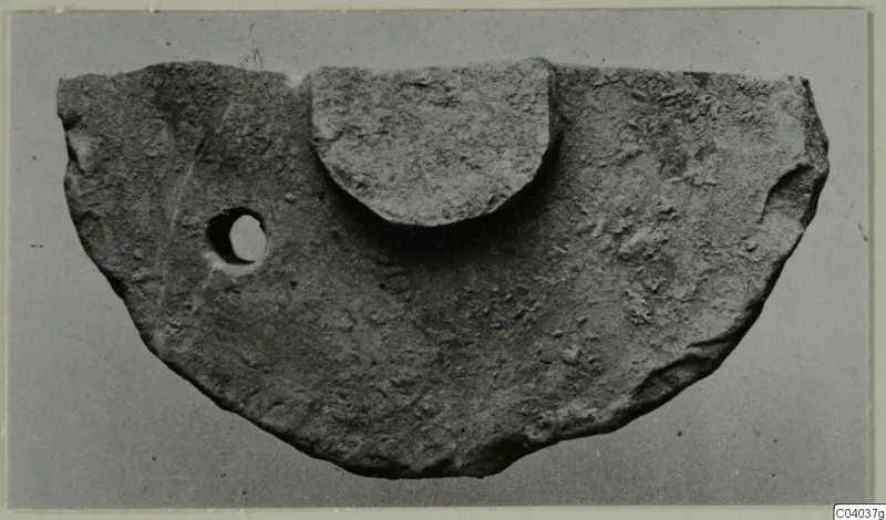 Half-disc shaped stone object with a small hole near one edge and a raised semicircular block on top