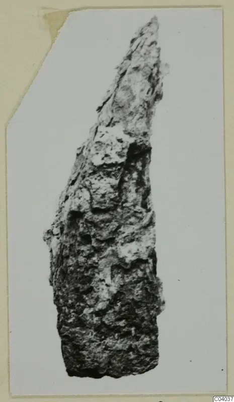 Corroded iron tool fragment, long and narrow, tapering to a point, shown on a photo mount