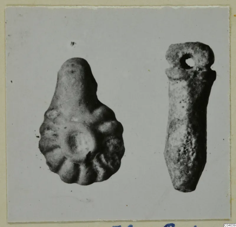 Two small finds on a card mount: a lobed pear-shaped piece and an elongated pendant with a hole at the top.