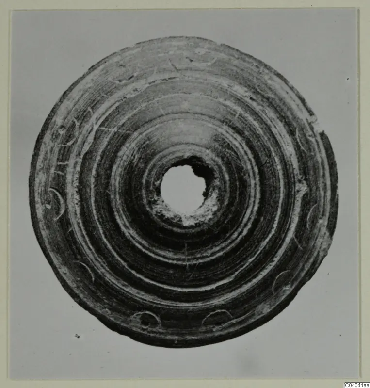 Flat disc with a central hole, concentric grooves and small crescent-shaped marks around the rim.