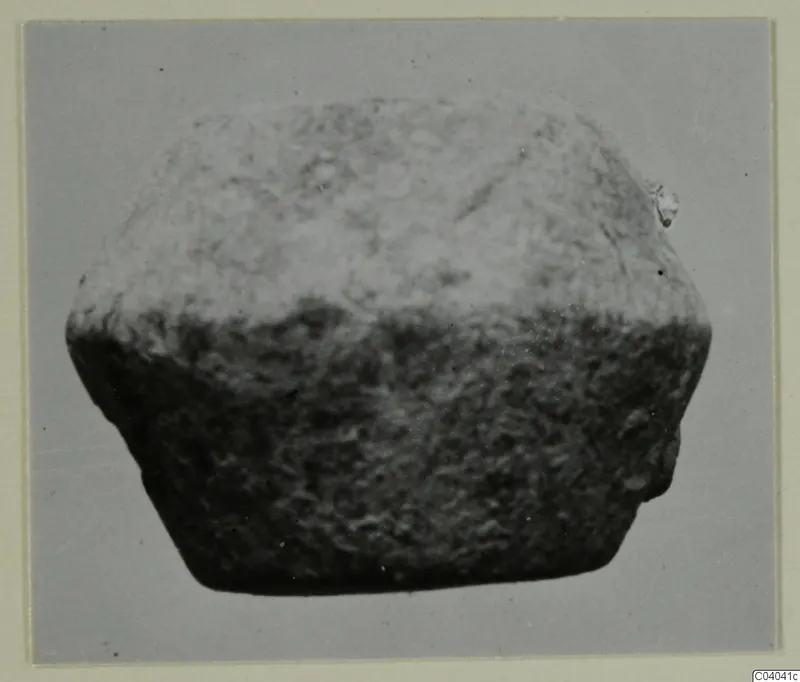 Small find: a squat, block-like object with a rough, granular surface, photographed against a grey background