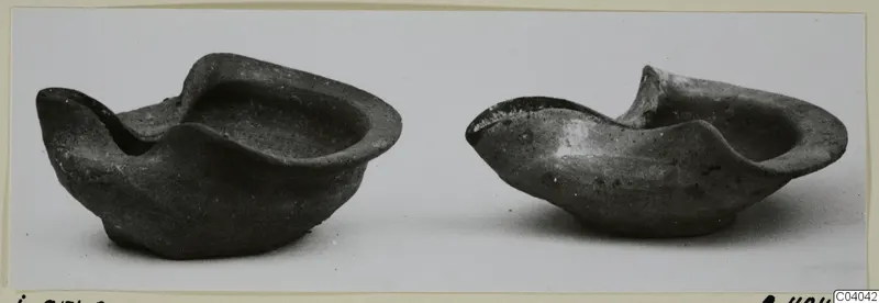 Two dark terracotta lamps with pinched spouts, photographed side by side