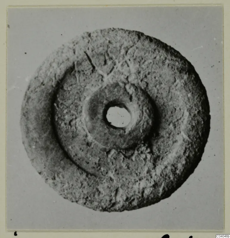 Flat disc-shaped bone object with a central hole, photographed from above against a grey backdrop