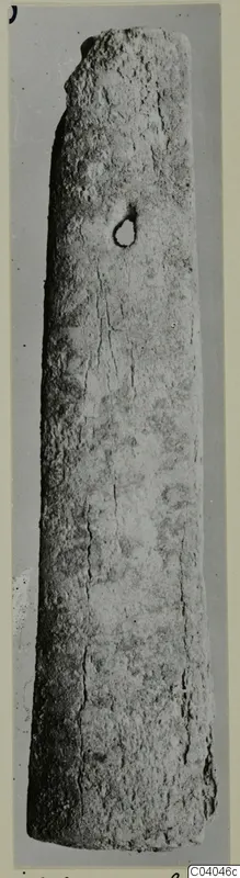 Long tapering bone object with a small hole near the upper end, photographed upright against a grey background