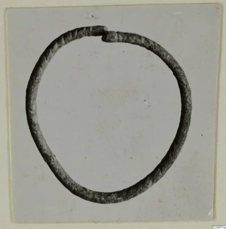 Bronze ring or bracelet, open with overlapping ends, shown in profile against a pale background