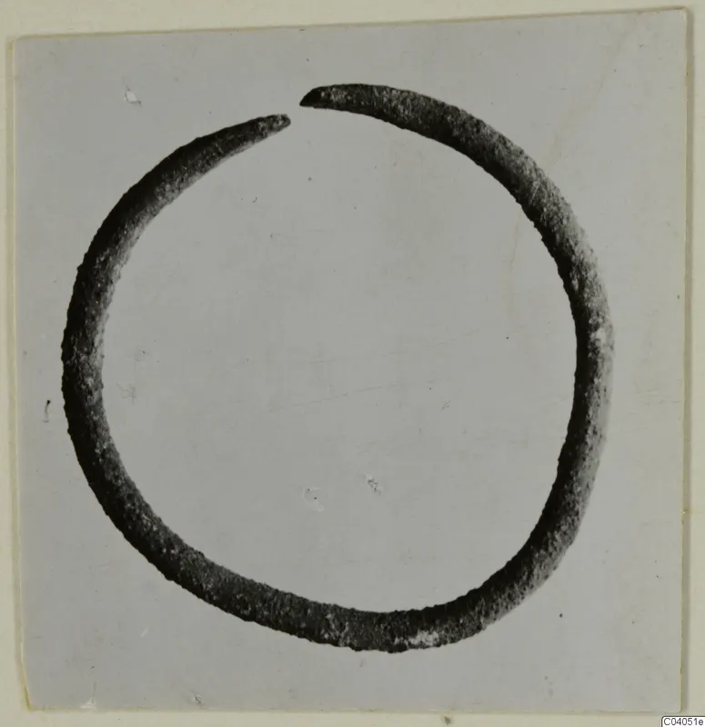 Open bronze ring or bracelet with a gap at the top, photographed on a grey card