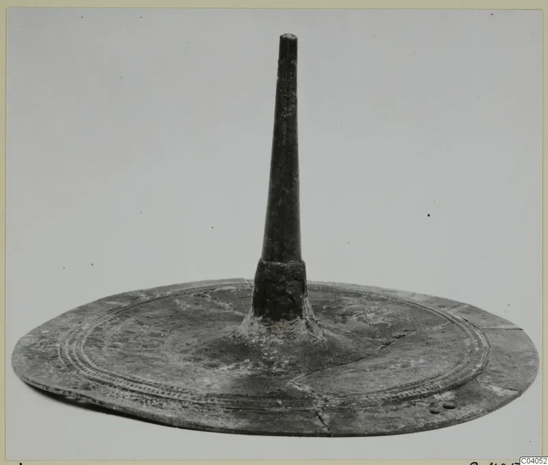 Bronze object: a flat circular disc with a tall tapering spike rising from its centre