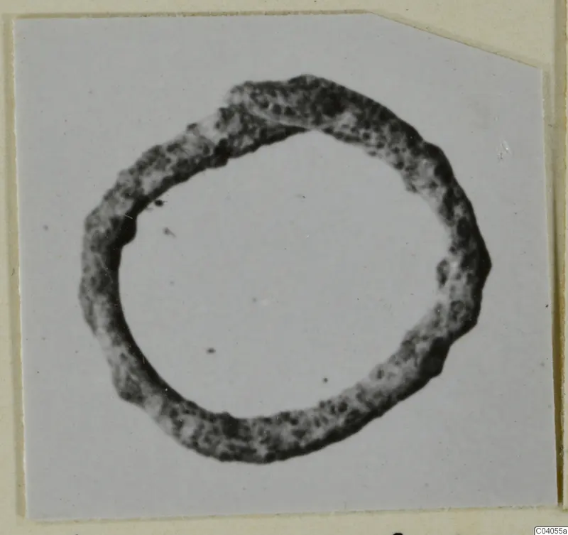 Bronze ring with a corroded, pitted surface, photographed flat on a pale card.