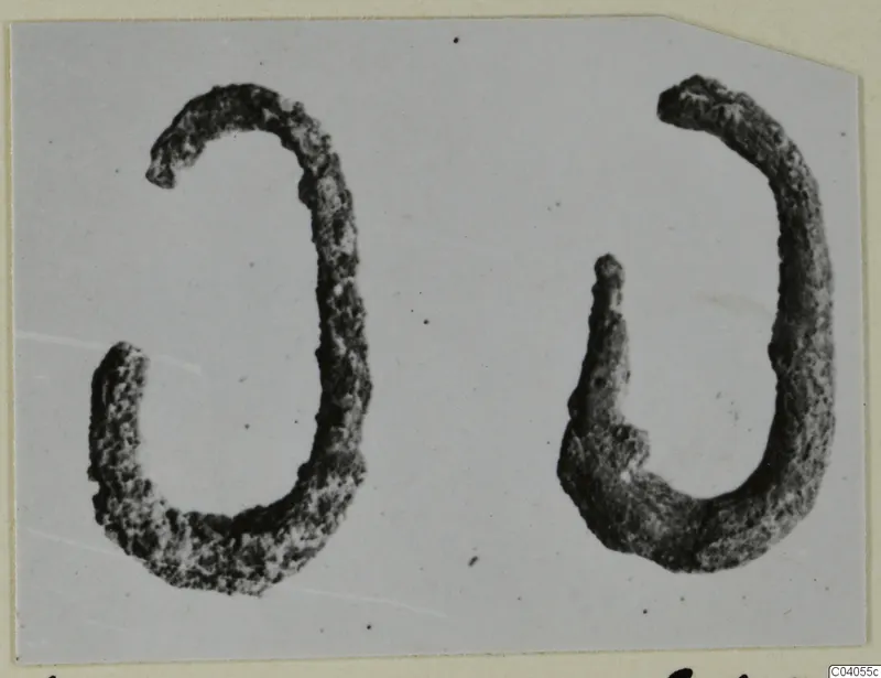 Two corroded curved bronze personal adornments, shown side by side.