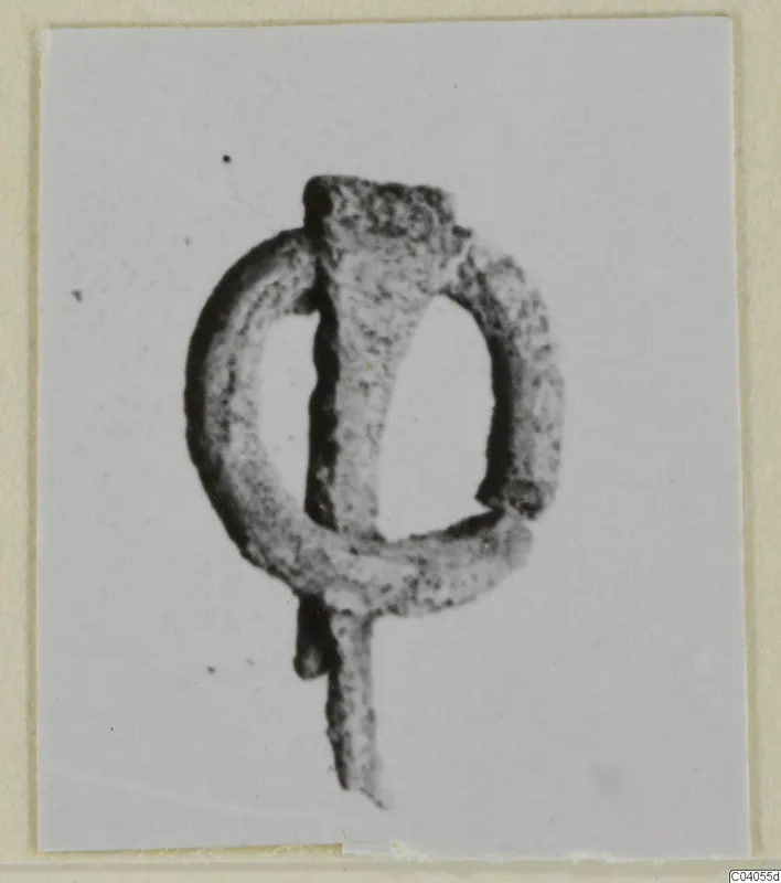 Small corroded bronze loop with a bar fixed across it, photographed on a pale card.